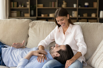 Joyful handsome young man resting on cozy sofa with loving sincere beautiful woman, enjoying pleasant conversation, spending leisure weekend time together in living room, communication concept.