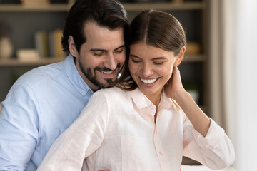 Head shot loving happy young caucasian man cuddling beautiful wife, showing tender affectionate feelings indoors. Dreamy cheerful millennial family couple enjoying peaceful moment together at home.