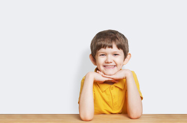 Child in a yellow T-shirt smiles and sits at the table.