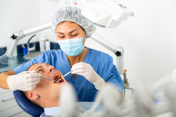 Professional asian female dentist examining male patient teeth with dental tools - mirror and probe