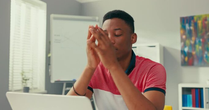 Young dark-skinned boy sits slumped in front of computer, props hands under face, bad news, losing money, overwork, sadness, fatigue, heartbreak, stress, disappointment
