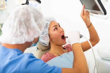 Professional dentist inspects asian female patient teeth with intraoral camera