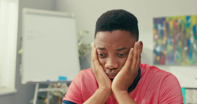 Handsome dark-skinned boy leans against the desk with hands leaning over the computer, carefully reads the article, email messages, has a focused face, serious, analyzes the text with understanding