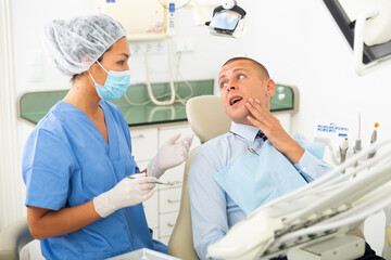Obraz premium Young businessman complains of toothache to female dentist at dental clinic office