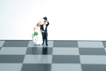 Wedding marriage strategy plan concept miniature people, toys photography. Bride and groom standing above chessboard isolated on white background.