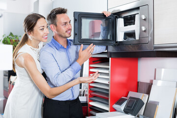 Happy young couple looking new microwave in furniture store