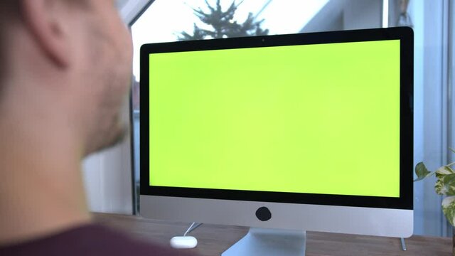 Caucasian Young Man using Green Screen on imac or computer in home office. Concept for online course, e learning, business to replace screen.