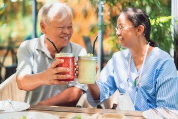 Asian old senior couples raise a glass of fruit juice to drink at cafe background on weekend...