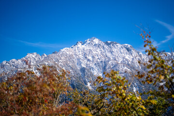 Fototapeta premium 富山県上市町にある雪が積もった晩秋のクズバ山の登山道から剣岳、大日岳、猫又山などを見る風景 A view of Mt. Kuzuba with snow on the trail in late autumn in Kamiichi Town, Toyama Prefecture, looking at Mt.Tsurugi, Mount Dainichi.
