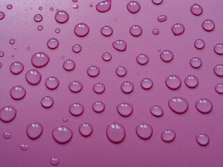 Transparent water drops on the violet plastic surface