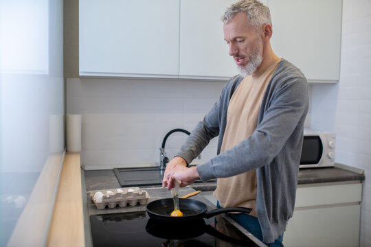 A Gray-haired Man Cooking Omlette In The Kitchen