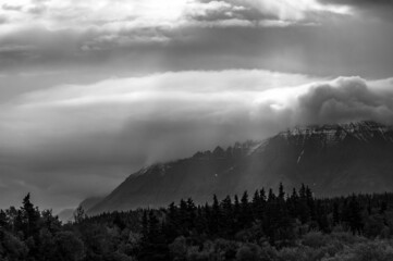 Dramatic black and white landscape with snow toped mountains, cloudy sky with sunbeams
