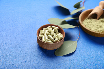 Bowls with powder, pills and green branch on color background, closeup