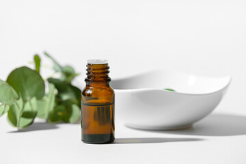 Bottle of essential oil and bowl on light background