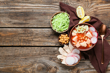 Bowl with delicious pozole soup and ingredients on wooden background