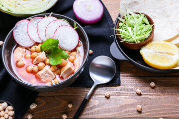 Bowl with tasty pozole soup and ingredients on wooden background