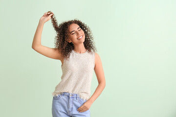Young African-American woman with healthy hair on green background
