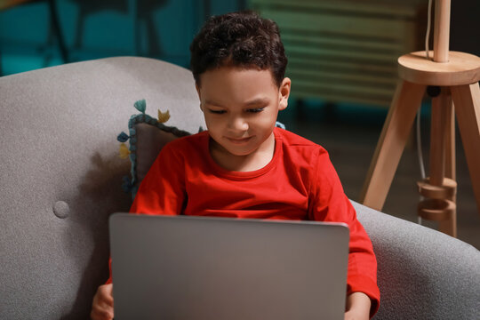 Little African-American boy watching cartoons on laptop at home late in evening
