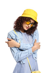 Young woman in stylish sunglasses wearing bucket hat and holding her shoulders on white background