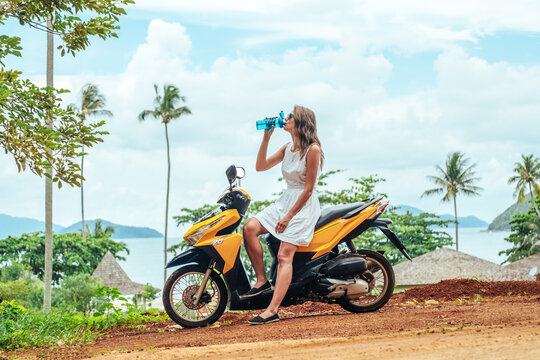 Portrait of young woman on scooter drinking water