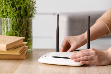 Woman inserting ethernet wire into wi-fi router on table in room - obrazy, fototapety, plakaty