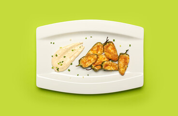 Plate with delicious jalapeno poppers and sauce on color background