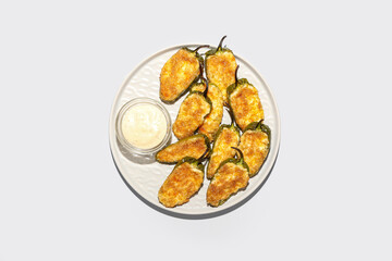 Plate with delicious jalapeno poppers and sauce on white background