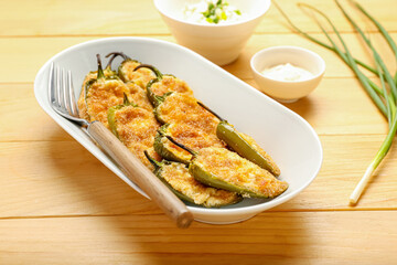 Plate with delicious jalapeno poppers and sauce on wooden background
