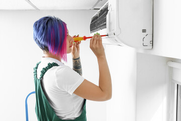 Female electrician repairing air conditioner in room