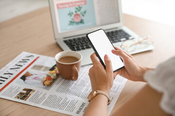 Woman using mobile phone on table with cup of coffee, newspaper and laptop - Powered by Adobe