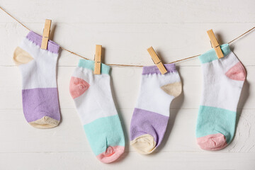 Many socks hanging on rope against light wooden background