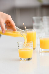 Woman pouring healthy juice from bottle into glass on table in room, closeup