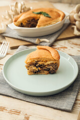 Plate with piece of tasty mushroom pot pie on white wooden background