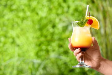 Woman holding glass of tasty Tequila Sunrise cocktail outdoors