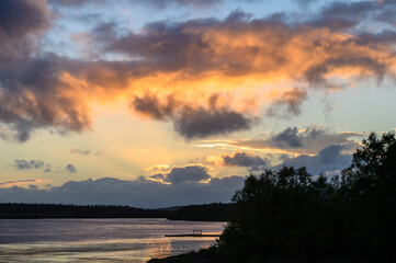 Dramatic sunset with light blue sky and bright clouds, and silhouetted tree line
