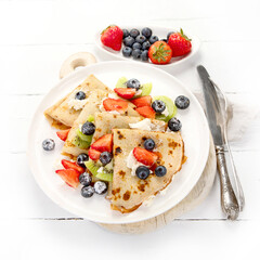 Sweet crepes with berries and cream on white wooden background.