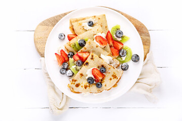 Sweet crepes with berries and cream on white wooden background.