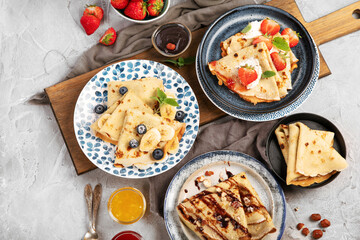 Sweet crepes assortment with berries chocolate on gray background.