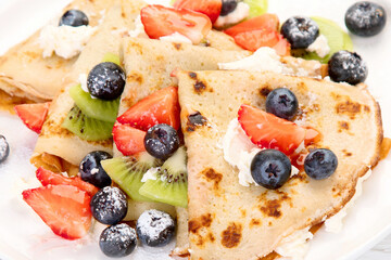 Sweet crepes with berries and cream on white wooden background.