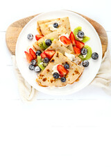 Sweet crepes with berries and cream on white wooden background.
