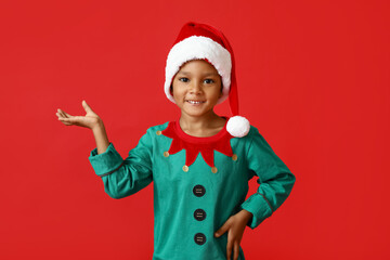 Little African-American boy in Santa hat showing something on red background