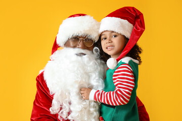 Little African-American girl with Santa Claus on yellow background