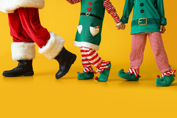 Legs of Santa Claus and little elves on yellow background