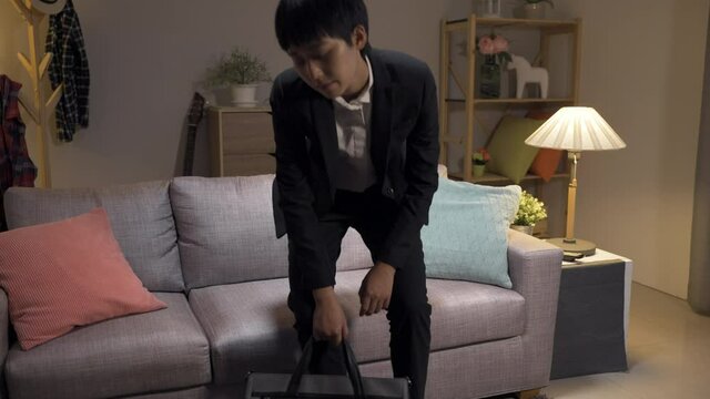 slow motion of exhausted asian businesswoman just arriving home is putting down her briefcase and slumping on the sofa in the living room at nighttime.
