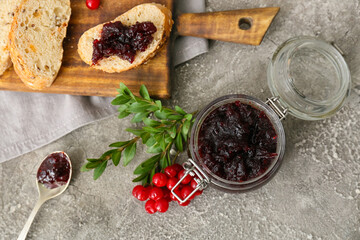 Jar of tasty lingonberry jam and toasts on grey background