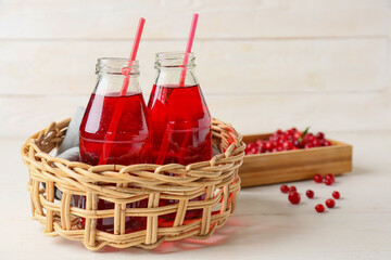 Basket with bottles of tasty lingonberry tea on light wooden background