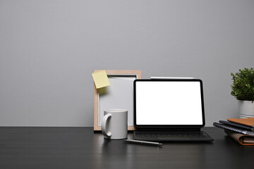 Home office desk with computer tablet, picture frame and coffee cup on black table.