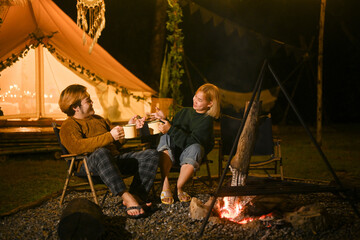 Happy young couple sitting near bonfire in the evening forest.