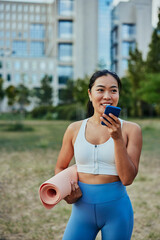 Asian sportswoman in tracksuit talking on mobile phone after exercising in park