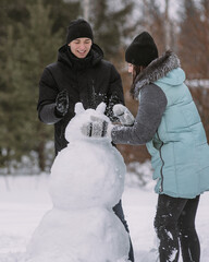 Couple of teenagers building snowman together in winter